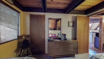 Een slaapkamer met een houten plafond, een dressoir met lades, een stoel en een bed met beddengoed met dessin.