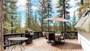 Una terrazza esterna con barbecue, tavolo e sedie, immersa tra alberi alti.