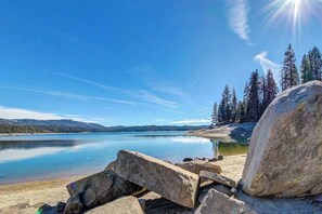 Ein ruhiger See bei klarem Himmel, umgeben von Bäumen und großen Felsen.