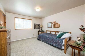Ein Schlafzimmer mit Bett, Kommode, Fenster und Nachttisch.