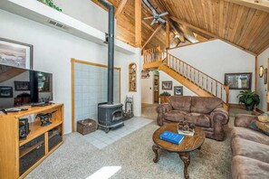 A spacious living room with a wooden ceiling, a fireplace, a staircase, and a leather sofa. - Sparrow Cove - East Village (Shaver Lake)