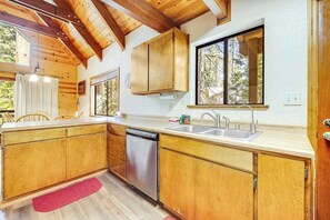 A kitchen with wooden cabinets, a dishwasher, a sink, and a window with a view of trees. - Tranquility In The Woods - Blue Lake Springs (Arnold)