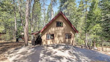 A two-story cabin with a red roof, surrounded by tall pine trees.