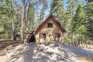 A two-story cabin with a red roof, surrounded by tall pine trees.