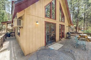 A wooden cabin with a covered patio, outdoor seating, and a large window. - Tranquility In The Woods - Blue Lake Springs (Arnold)