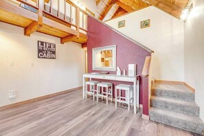 A cabin interior with a wooden staircase, a desk with stools, and a mirror.