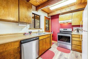 A compact kitchen with wooden cabinets, a dishwasher, an oven, and a refrigerator. - Tranquility In The Woods - Blue Lake Springs (Arnold)