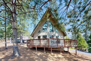 Eine Holzhütte mit einer Holzterrasse und großen Fenstern, umgeben von Bäumen.