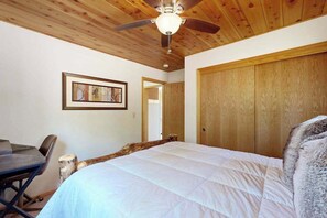 Ein Schlafzimmer mit einem Bett, einem Deckenventilator, einem gerahmten Bild an der Wand und einer Holztür.