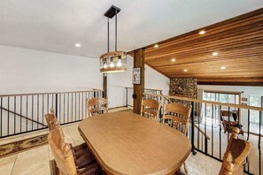 A dining area with a large wooden table and chairs, a hanging light fixture, and a stone accent wall.