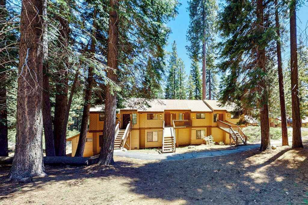 Un chalet à deux étages, avec une façade en bois, entouré de grands pins.