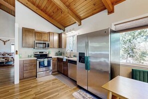 A modern kitchen with wooden cabinets, stainless steel appliances, and a view of the outdoors. - Green Abode - Pine Mountain Lake (Groveland)