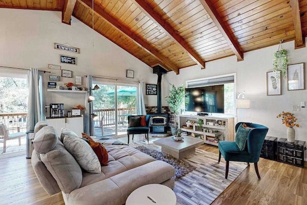 A spacious living room with a high ceiling, a fireplace, a television, and a comfortable seating area. - Green Abode - Pine Mountain Lake (Groveland)
