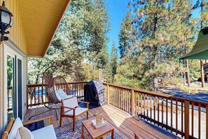 A wooden deck with outdoor furniture, a barbecue grill, and a view of pine trees. - Green Abode - Pine Mountain Lake (Groveland)