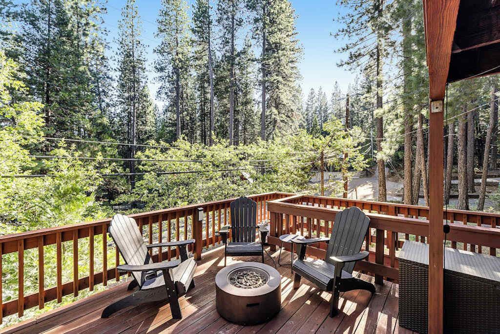 A wooden deck with Adirondack chairs and a fire pit, overlooking a forested area.