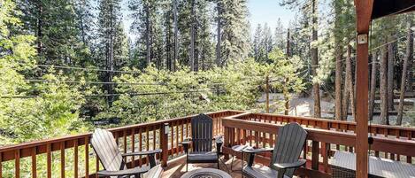 A wooden deck with Adirondack chairs and a fire pit, overlooking a forested area.