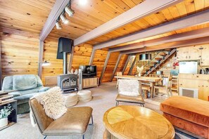 Ein gemütlicher Raum mit Holzwänden, einem Kamin, einem Fernseher und einer Essecke.