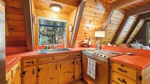 A wooden cabin kitchen with a large window, a stove, and a sink. - Heavenly Daze - Meadowmont (Arnold)