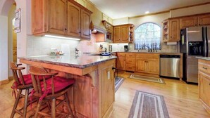 A kitchen with wooden cabinets, a stainless steel refrigerator, and a bar area with stools. - New England Cottage - Ockenden Ranch (Shaver Lake)