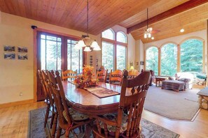 A dining area with a wooden table and chairs, large windows, and a ceiling fan. - New England Cottage - Ockenden Ranch (Shaver Lake)