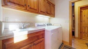 A kitchen with wooden cabinets, a white countertop, a sink, and a washing machine. - New England Cottage - Ockenden Ranch (Shaver Lake)