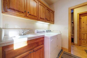A kitchen with wooden cabinets, a white countertop, a sink, and a washing machine. - New England Cottage - Ockenden Ranch (Shaver Lake)