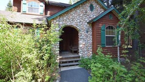 A rustic cabin with a stone archway entrance, wooden siding, and a small porch. - New England Cottage - Ockenden Ranch (Shaver Lake)
