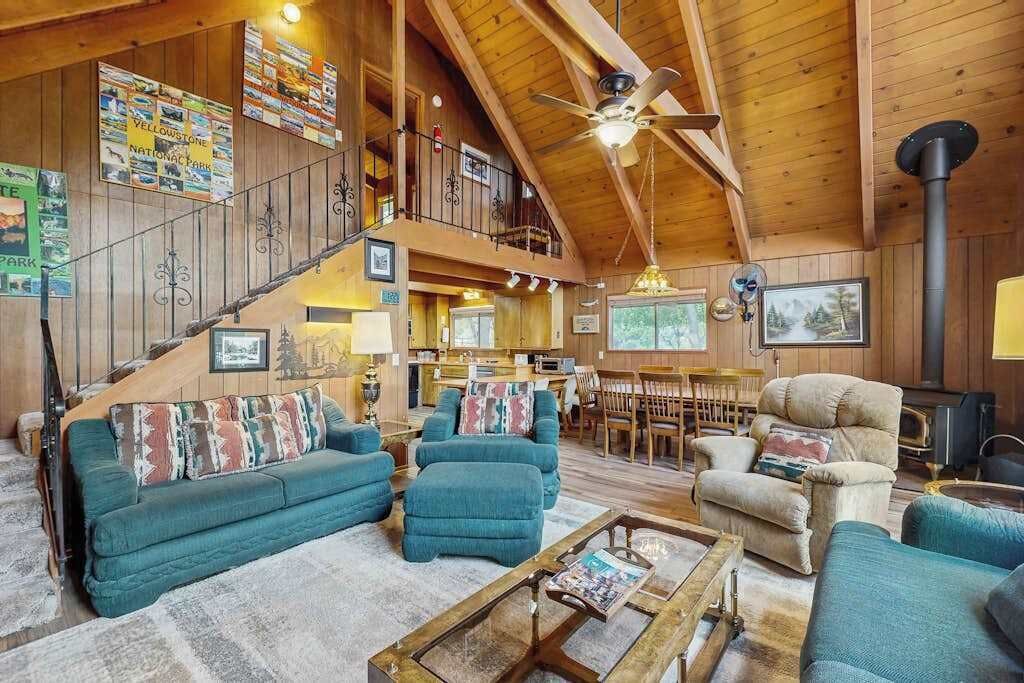 A spacious living area with a high ceiling, wooden beams, a central fireplace, and a staircase leading to an upper level.