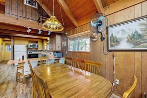 A wooden interior with a dining table, chairs, a kitchen area, and a fan.