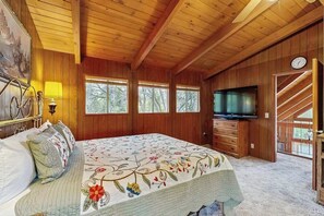 A wooden-paneled bedroom with a bed, a television, and a clock on the wall.