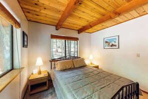 Ein Schlafzimmer mit einem Bett, zwei Nachttischen, einem Fenster und einer Holzbalkendecke.