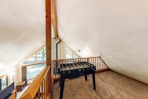 A room with a foosball table, a TV, and a staircase leading to a loft area. - The Arrow House - Big Tree Village (Camp Connell)
