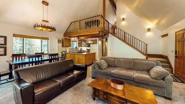 A spacious living area with a staircase, leather sofas, a wooden coffee table, and a kitchen in the background. - The Arrow House - Big Tree Village (Camp Connell)
