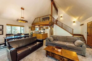 A spacious living area with a staircase, leather sofas, a wooden coffee table, and a kitchen in the background. - The Arrow House - Big Tree Village (Camp Connell)