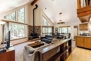 A spacious living area with a fireplace, a sofa, a television, and a dining area with a table and chairs. - The Arrow House - Big Tree Village (Camp Connell)
