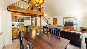 A spacious living area with a wooden dining table, a sofa, and a television. - The Arrow House - Big Tree Village (Camp Connell)