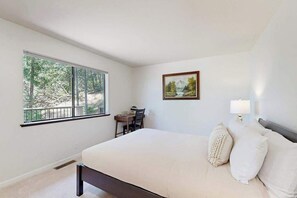 A bedroom with a large bed, a desk, and a window with a view of trees.