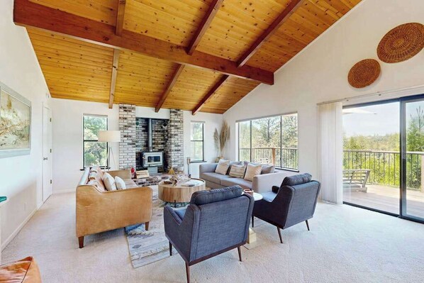 A spacious living area with a high ceiling, a fireplace, and large windows.