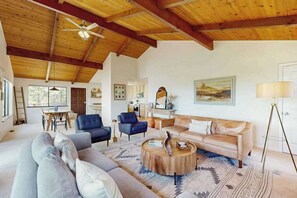 A spacious living room with a high ceiling, a large sofa, a coffee table, and a painting on the wall.