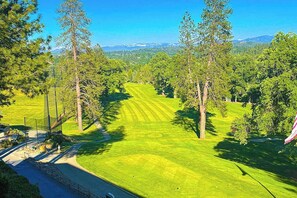 Campo de golf con un camino despejado, rodeado de árboles y vistas a montañas lejanas.