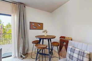 Una habitación con una mesa redonda de madera, dos taburetes, un sofá, un cuadro en la pared y un balcón con vistas.