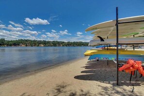 Paisatge amb un llac, canoes i kayaks amarrats a una platja de sorra.