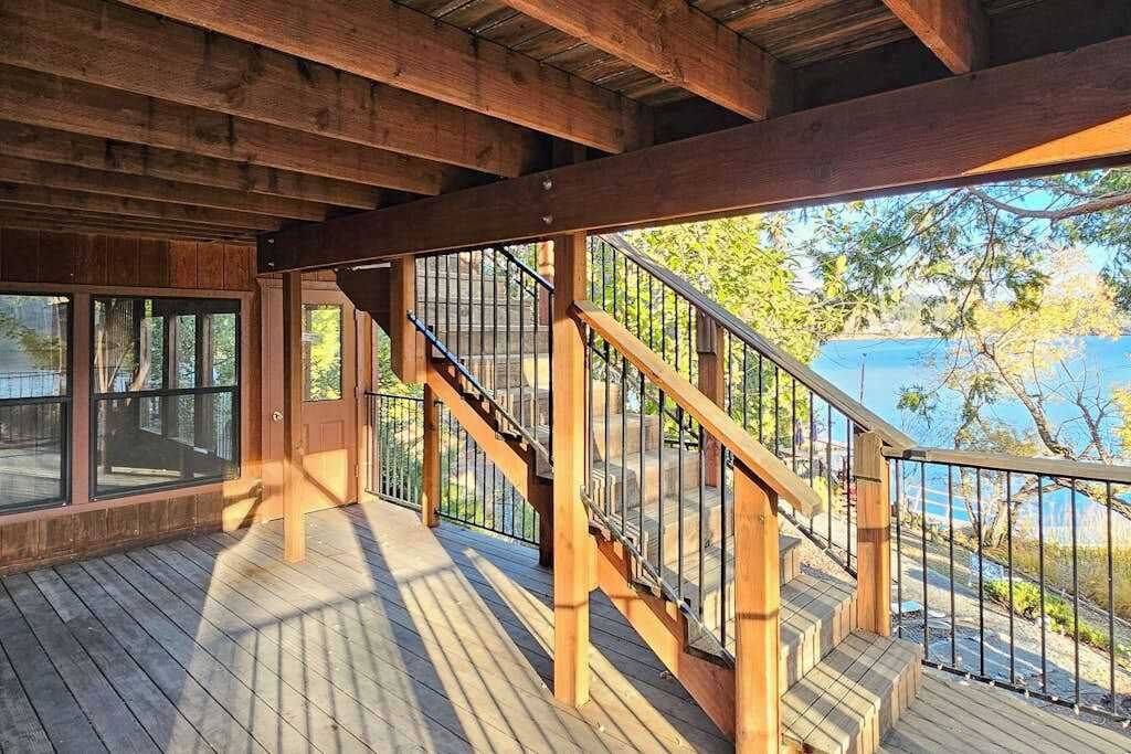A wooden deck with a staircase leading to a covered area with large windows.