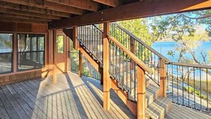 Una terraza de madera con una escalera que lleva a una zona cubierta con ventanales grandes.