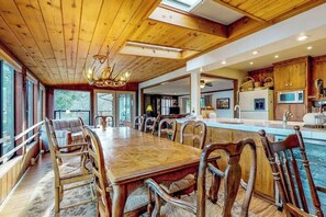 A spacious dining area with a long wooden table and chairs, a kitchen with modern appliances, and large windows providing natural light. - Heart's Desire on the Lake - Pine Mountain Lake (Groveland)
