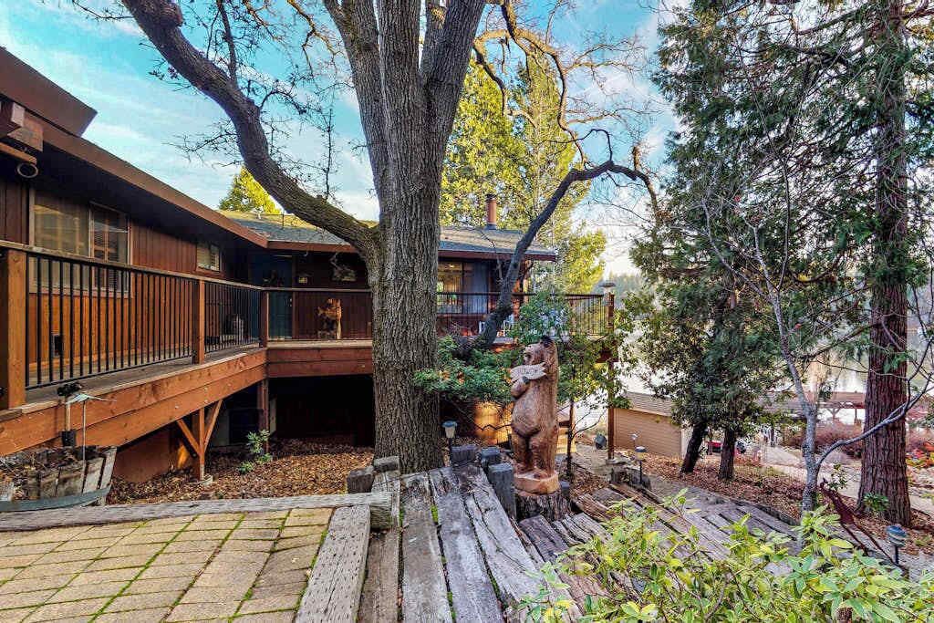 A wooden cabin with a deck, surrounded by trees and a bear statue.