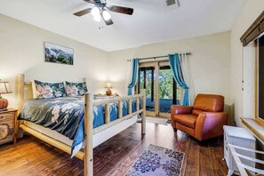 A bedroom with a bed, a chair, a window with curtains, a ceiling fan, and a nightstand with a lamp.