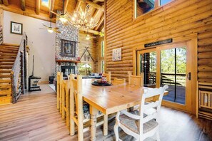 A log cabin interior with a dining area, stone fireplace, and a large window.