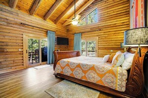 A log cabin bedroom with a bed, a ceiling fan, and a television mounted on the wall. - The Cub Inn - Groveland (Groveland)