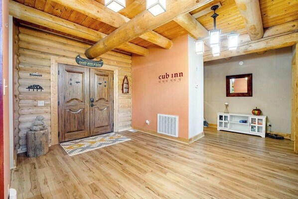 A log cabin interior with a wooden floor, a sign reading 'CUB INN,' and a white console table.